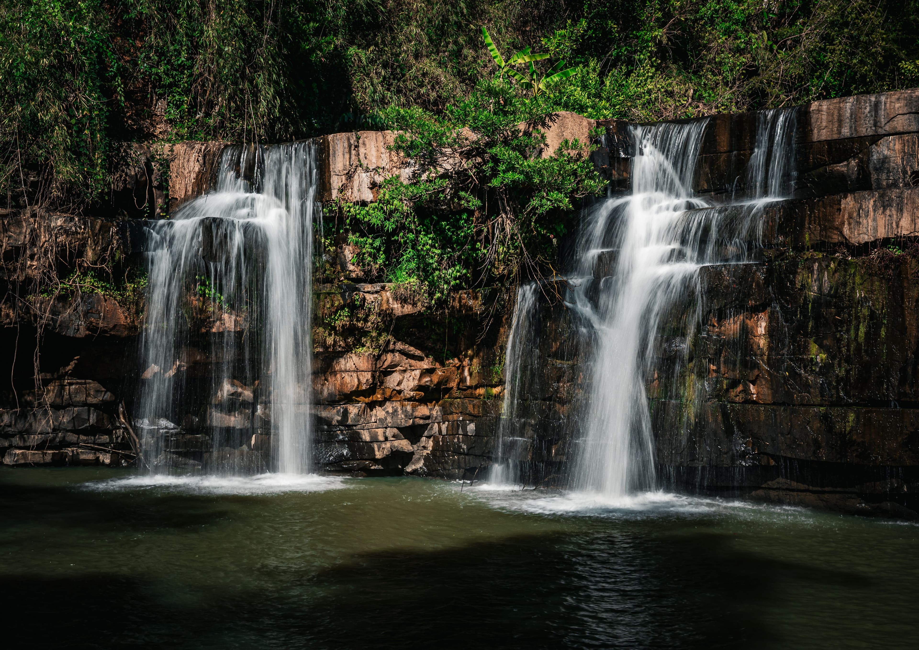 Waterfalls flowing over layered rock surrounded by green foliage
